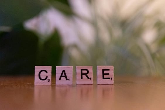 Close-up of wooden tiles spelling 'CARE' on a table with a blurred background, evoking a sense of support.